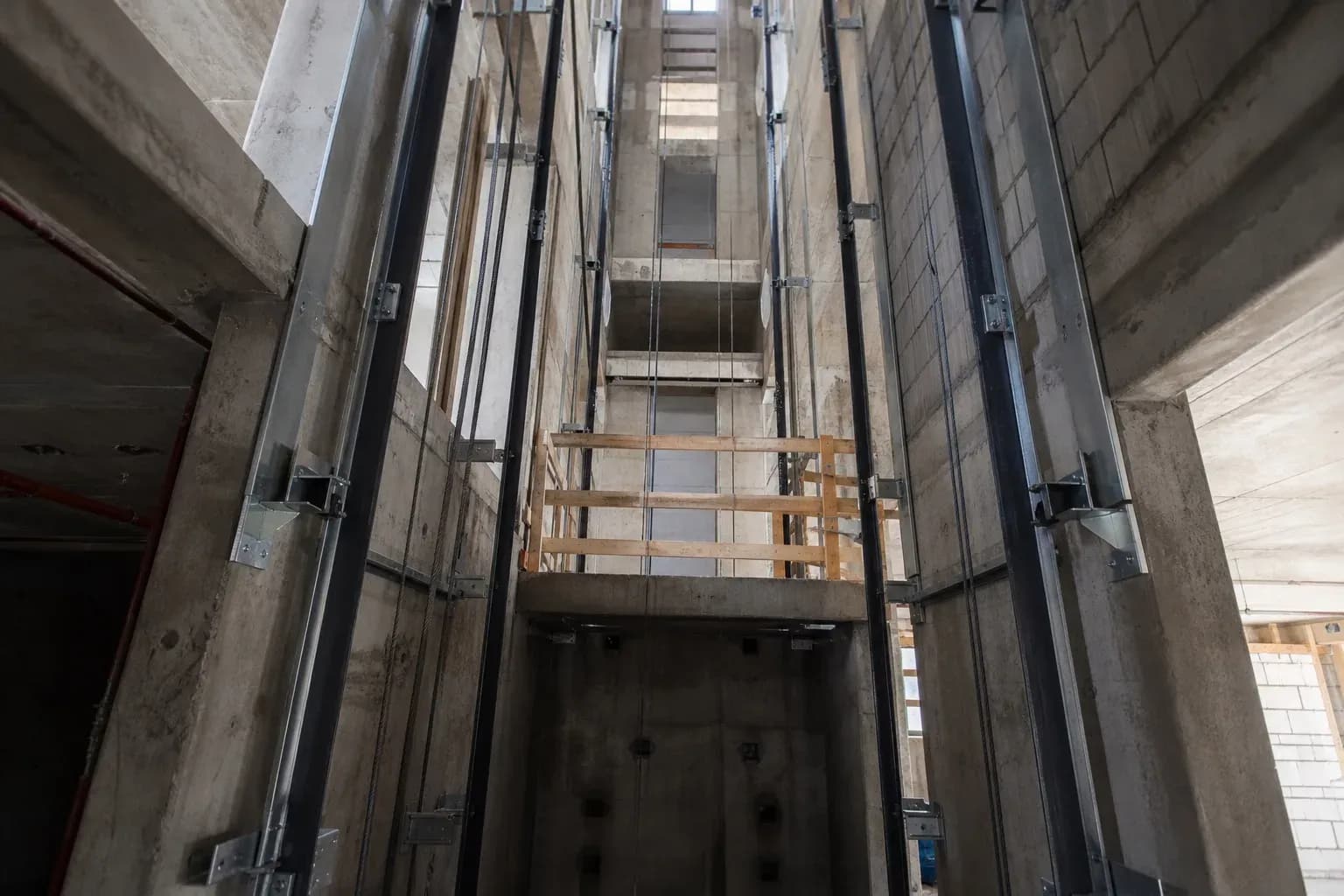 چاه آسانسور ناتمام با ریلهای راهنما و داربست موقت؛ نشاندهنده کارهای عمرانی مؤثر بر قیمت آسانسور